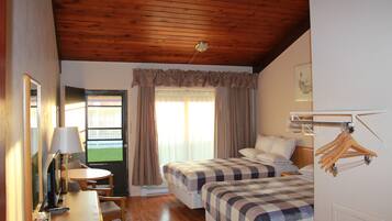 Habitación de hotel con dos camas, un escritorio con lámpara, una silla, una ventana con cortinas y un perchero.
