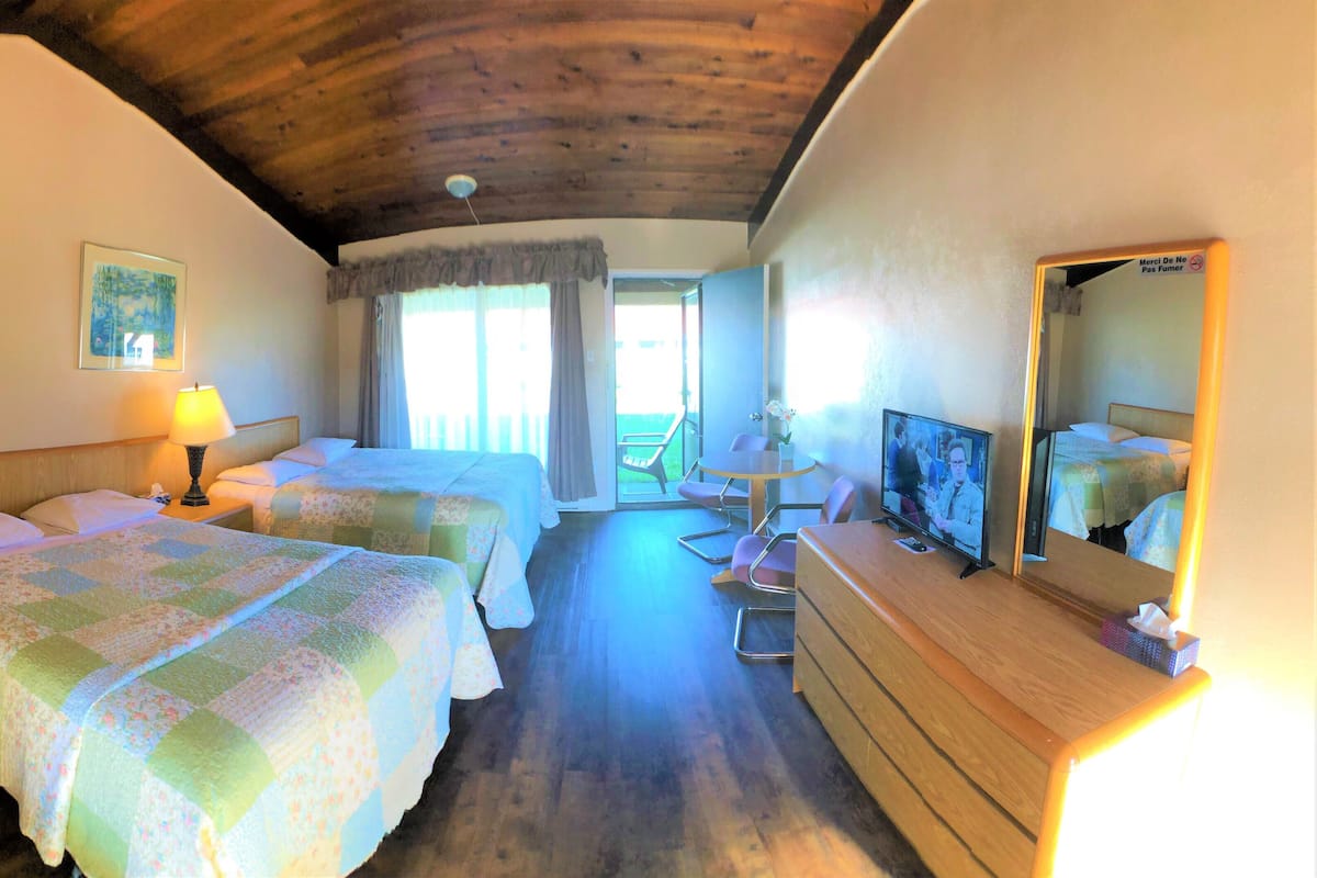 A hotel room with two beds, a wooden ceiling, a TV, and a balcony with chairs.
