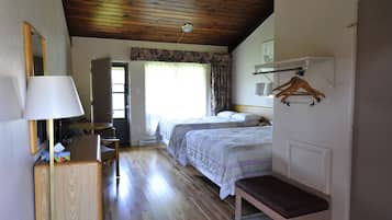 Una habitación con dos camas, un escritorio con lámpara, un banco, techo de madera y una puerta que da a otra habitación.