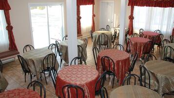 Un comedor con varias mesas redondas cubiertas con manteles estampados, rodeado de sillas de metal.