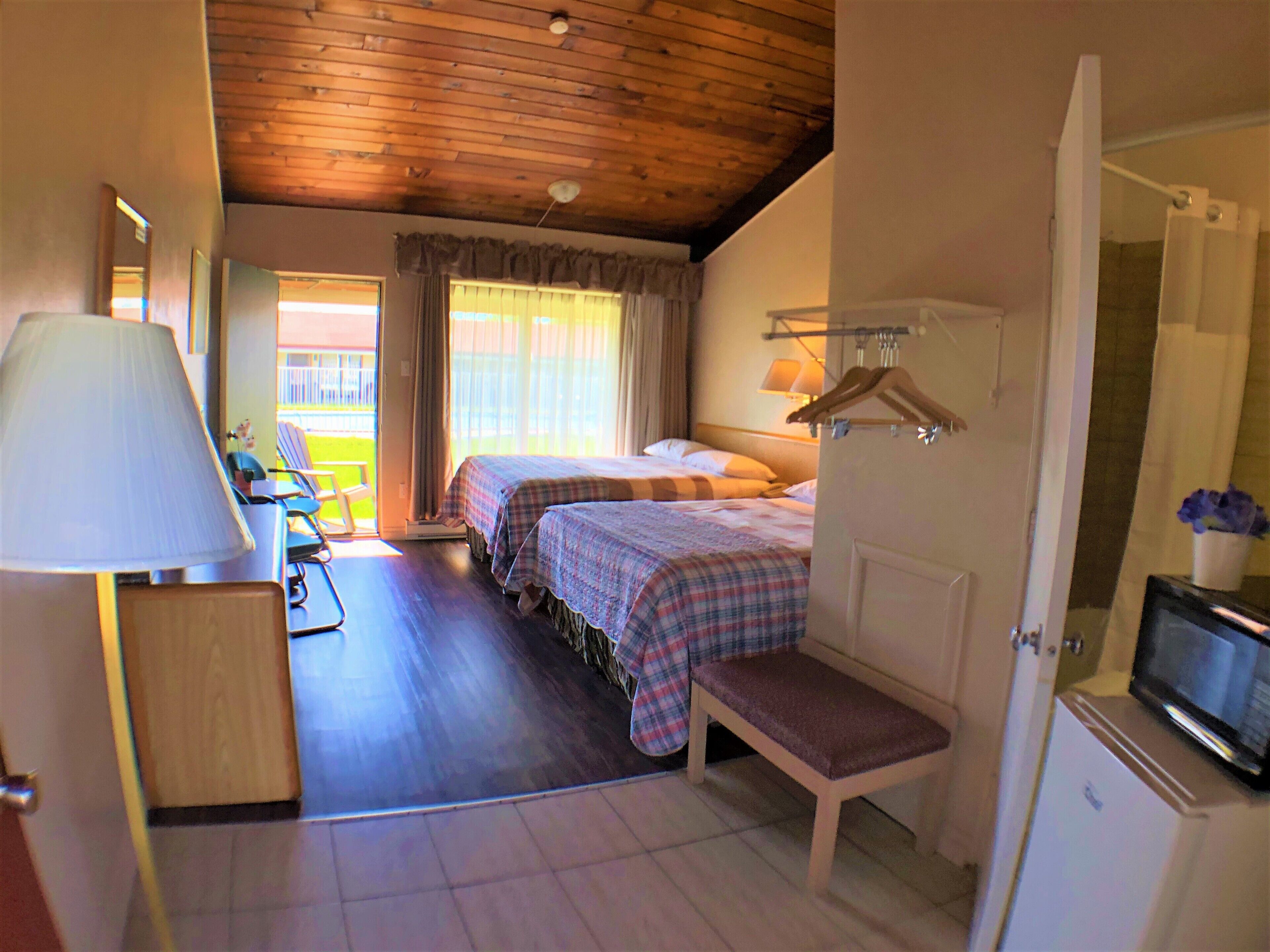 A hotel room with two beds, a bench, a TV, and a desk with a lamp.