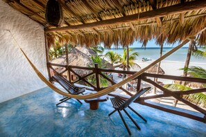 A hammock chair setup under a thatched roof, overlooking a beach with palm trees and a boat. - Beachfront Hotel La Palapa - Adults Only (Isla Holbox)