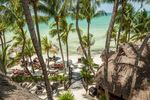 Un resort en la playa con cabañas de techo de paja, palmeras y sillas de descanso.