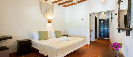A bedroom with a bed, bedside tables, a nightstand, a dresser, a mirror, a chandelier, and a door leading to another room.