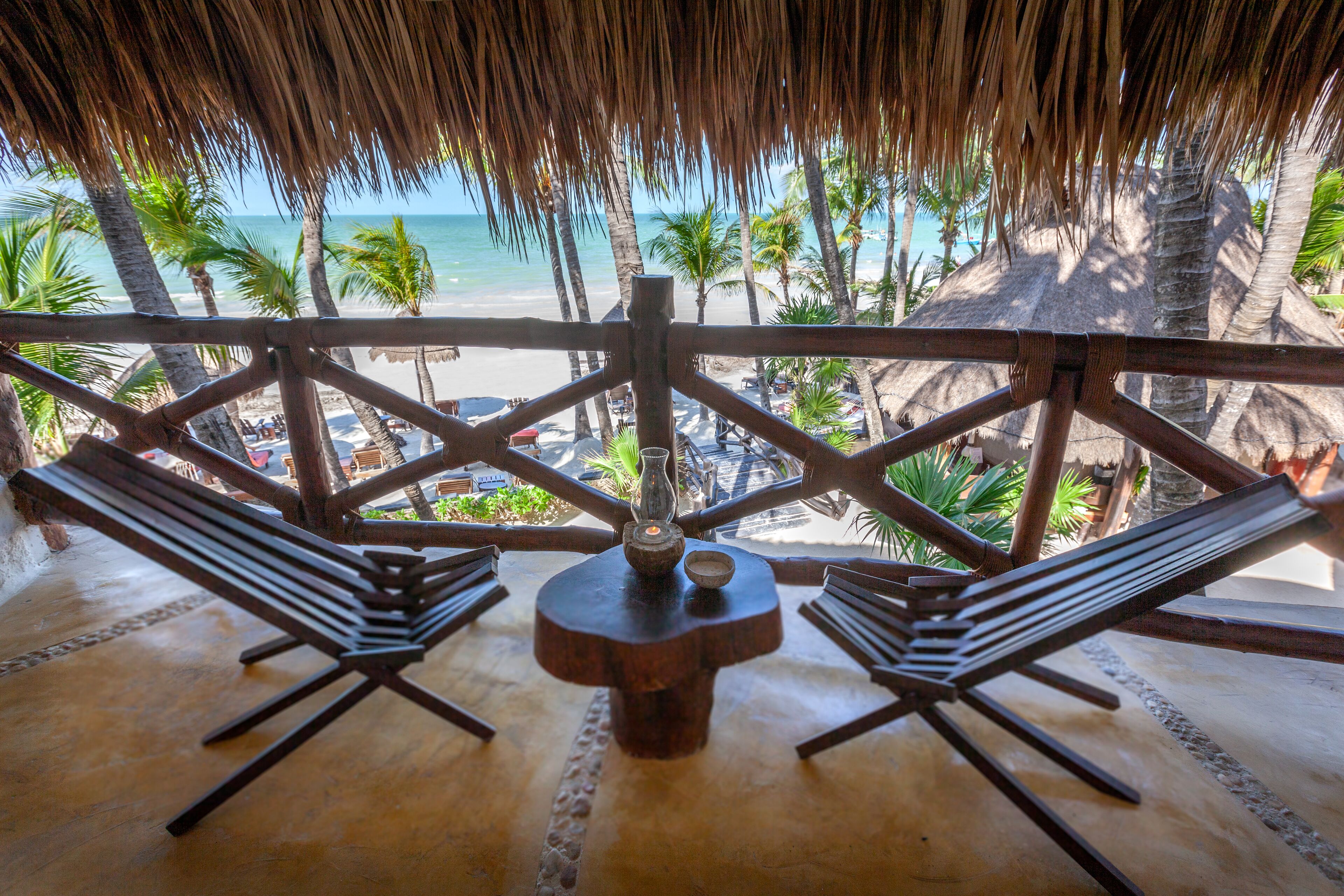 A wooden table with two benches, a thatched roof, and a view of the beach and palm trees.
