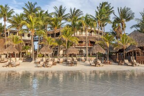 A beachfront resort with thatched-roof structures, palm trees, and sun loungers. - Beachfront Hotel La Palapa - Adults Only (Isla Holbox)