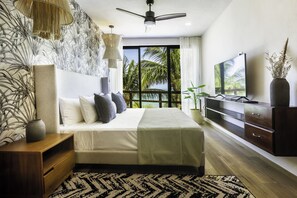 A modern bedroom with a large bed, a TV, and a view of palm trees. - Beachfront Hotel La Palapa - Adults Only (Isla Holbox)