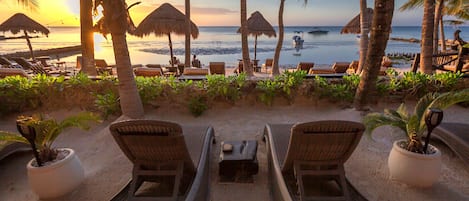 Un área de descanso frente a la playa, con sillones y sombrillas de paja, con vista al océano.