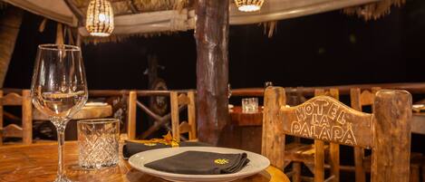 A dining table with a glass, a plate, and a napkin, set in a wooden chair with a sign reading "HOTEL LA PALAPA".