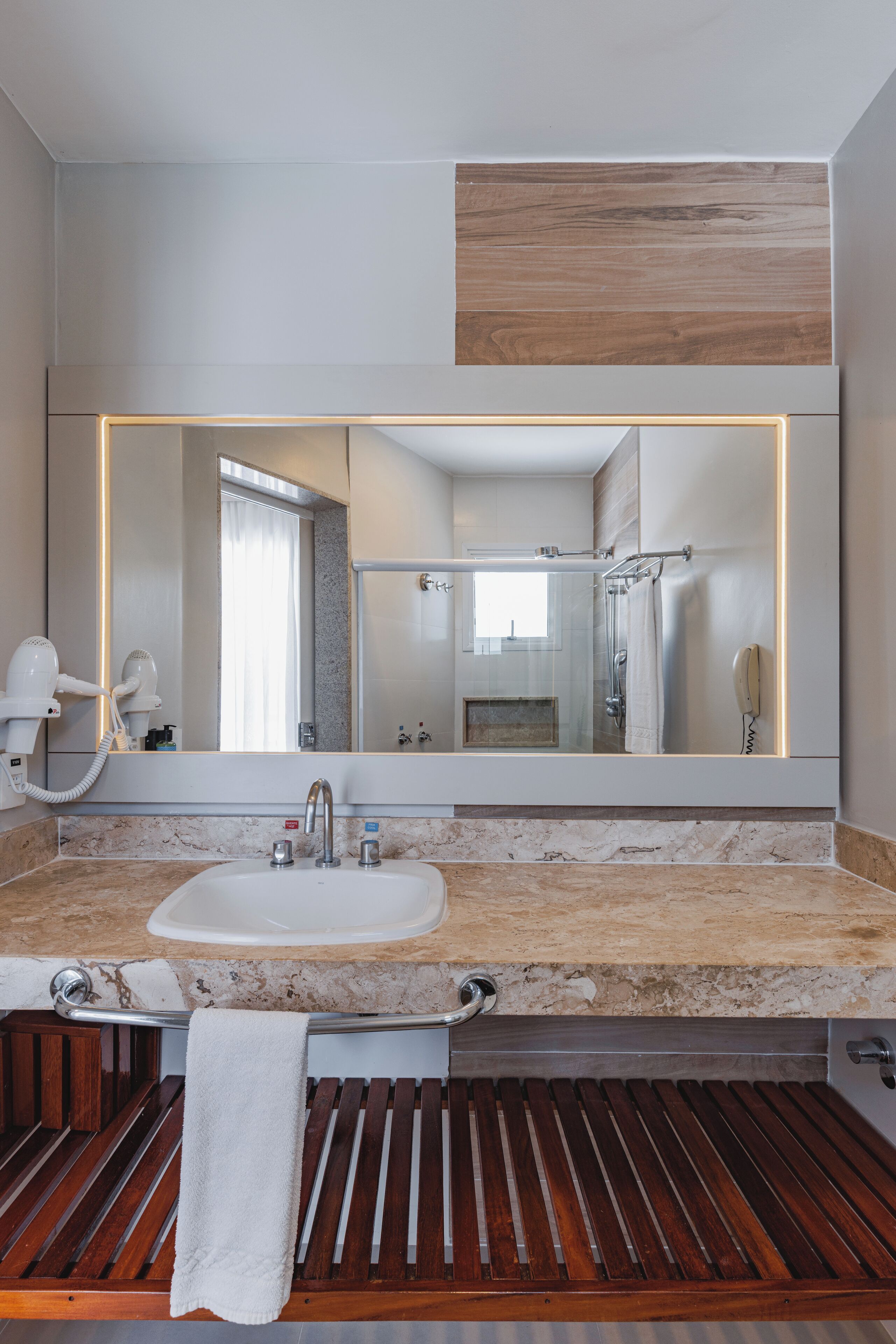 A modern bathroom with a large mirror, a sink, a towel rack, and a shower area.
