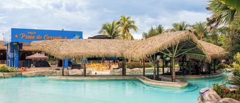 A pool area with a thatched-roof structure, palm trees, and a sign for 'Praia do Cerrado.'