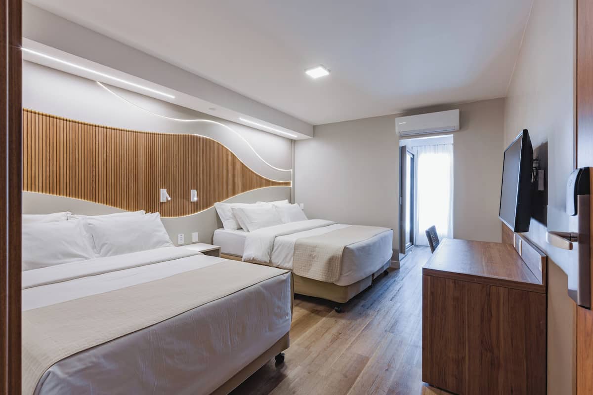 Une chambre d’hôtel avec deux lits, une tête de lit en bois, un téléviseur à écran plat et une armoire en bois.
