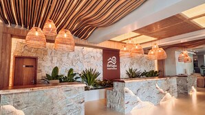 A lobby with a stone wall, wooden reception desk, and hanging wicker lamps. - Rio Quente Resorts Refúgio Grand Premium – Antigo Hotel Turismo (Rio Quente)