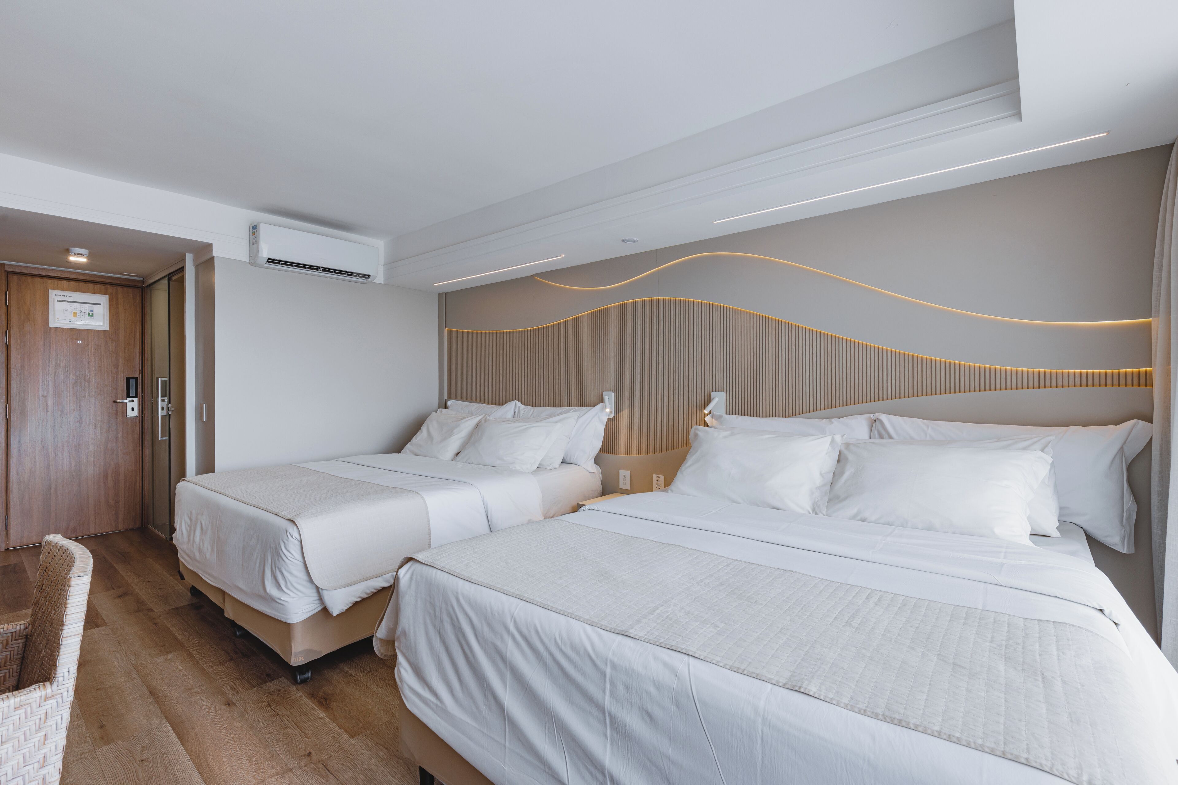 Een hotelkamer met twee bedden, een houten vloer, een wandairconditioner en een modern plafondontwerp.