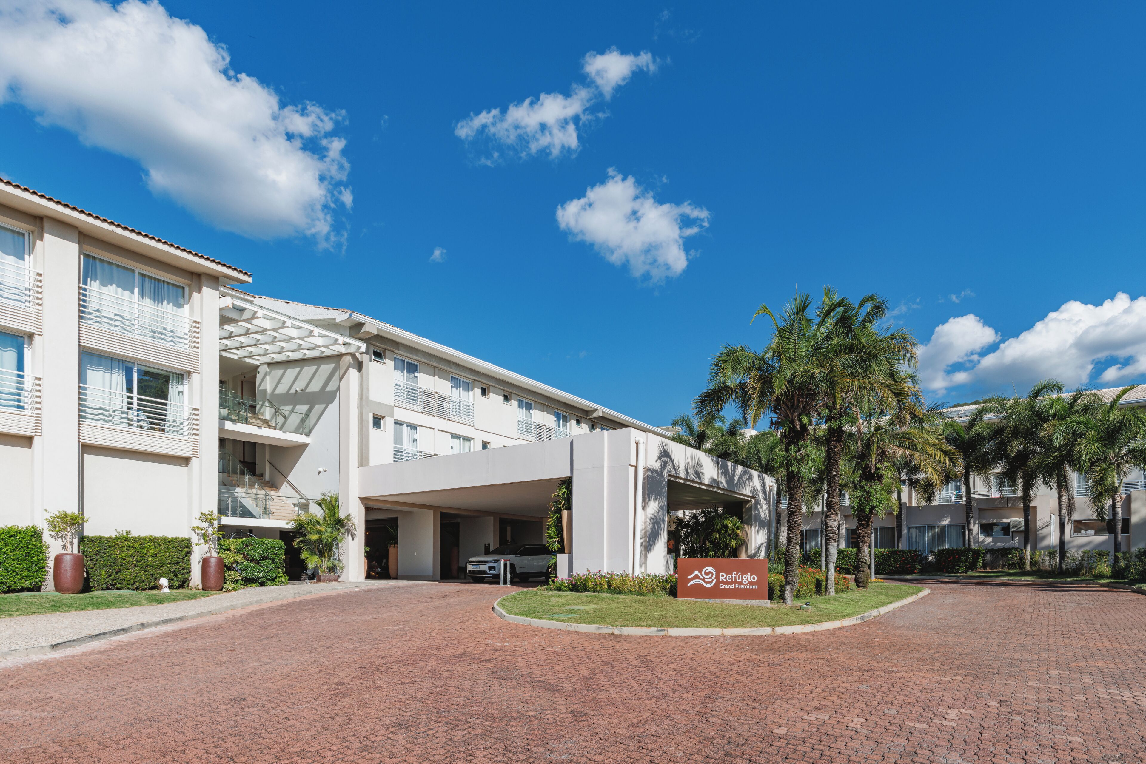 A modern hotel with a covered entrance, palm trees, and a clear blue sky.