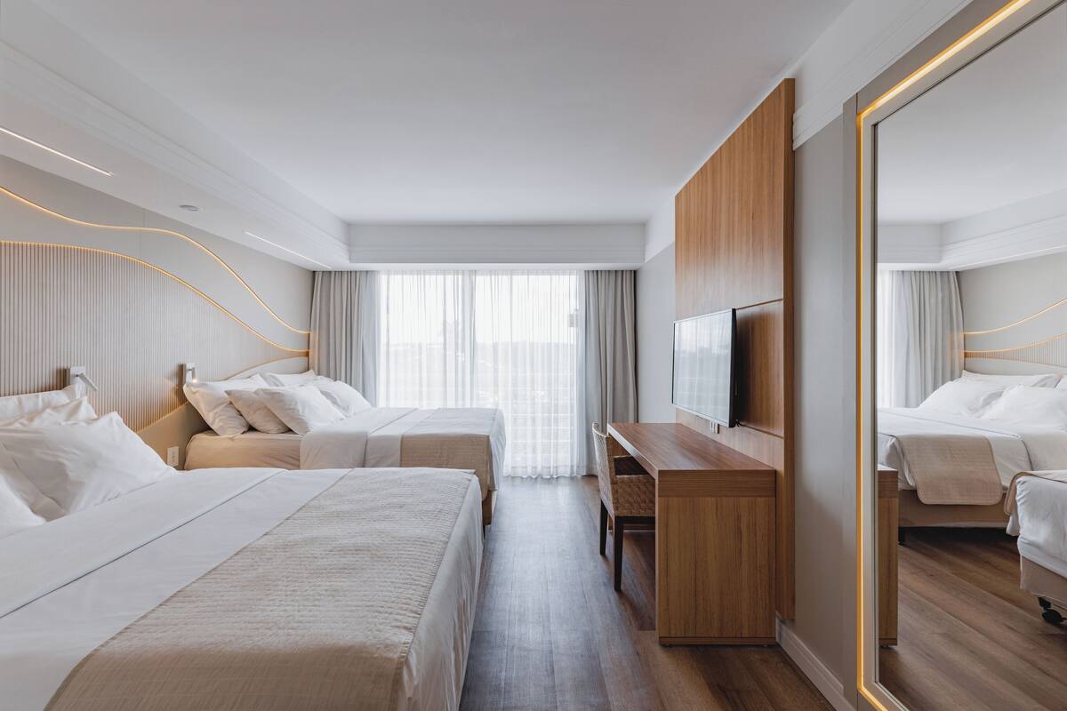 Une chambre d’hôtel moderne avec deux lits, un bureau en bois, un grand miroir et une télévision.