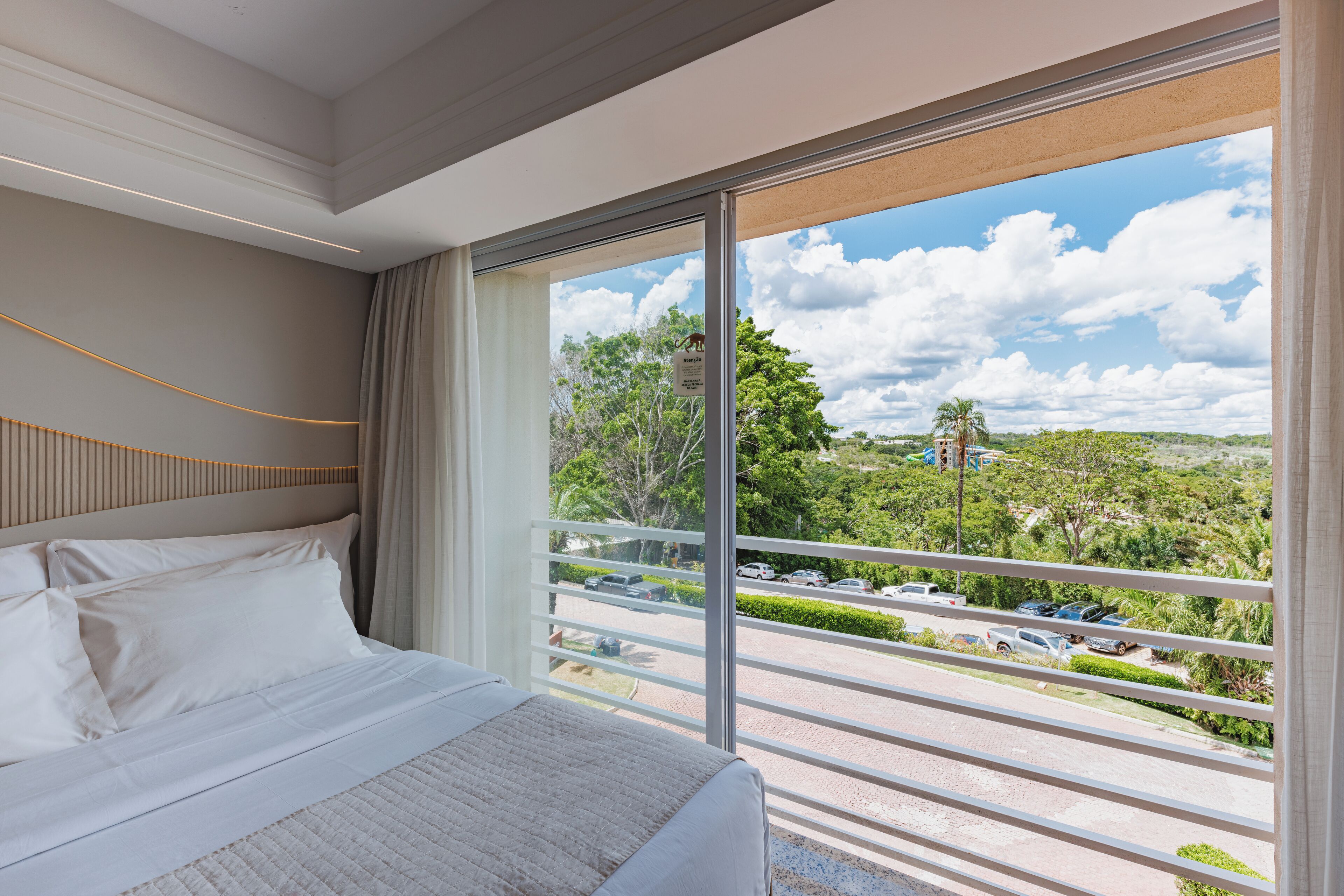A hotel room with a large bed, a view of a parking area, and a balcony with a railing.