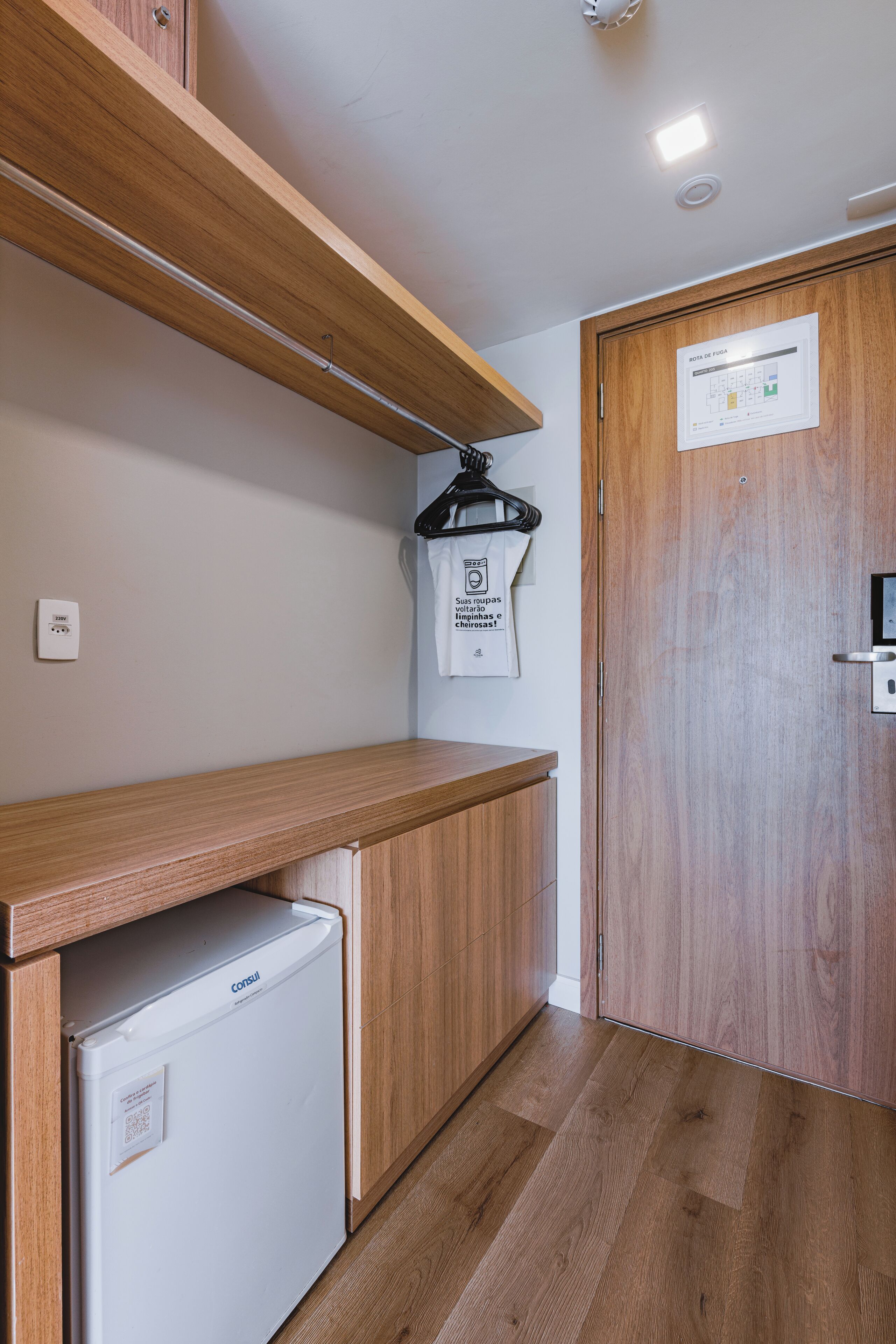 Cozinha compacta com bancada de madeira, geladeira embutida e porta de madeira com um aviso.