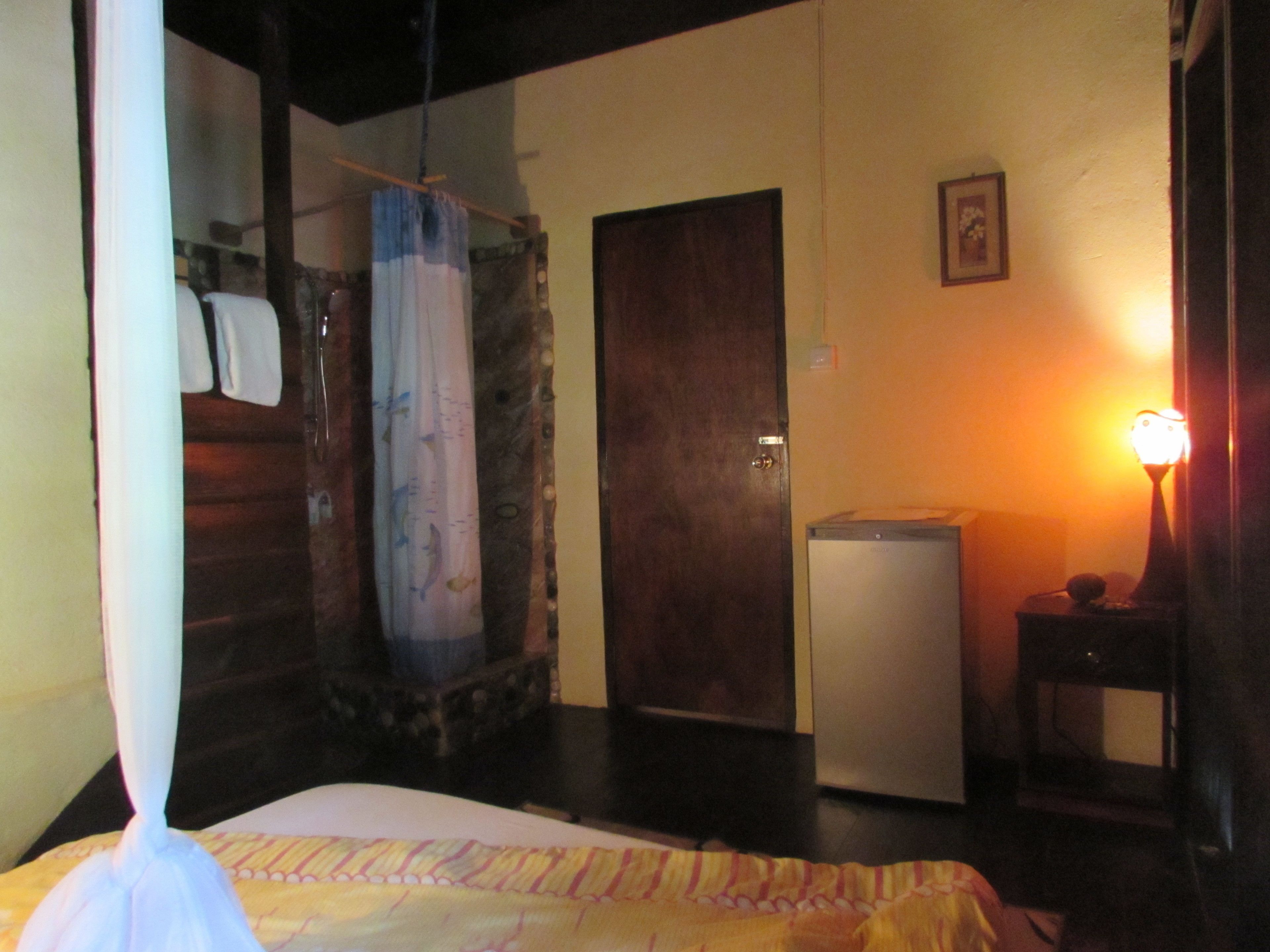 A bedroom with a bed, a wardrobe, a small table with a lamp, and a door.
