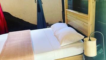 Ein ordentlich bezogenes Bett mit weißen Leinen, einem Holzkopfteil und einer Nachttischlampe.