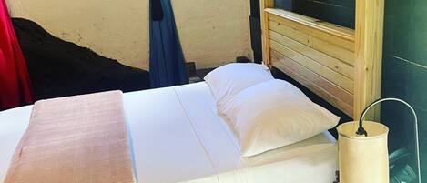 A neatly made bed with white linens, a wooden headboard, and a bedside lamp.
