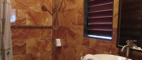 A bathroom with a marble tile wall, a shower, a toilet, and a sink with a towel hanging on it.