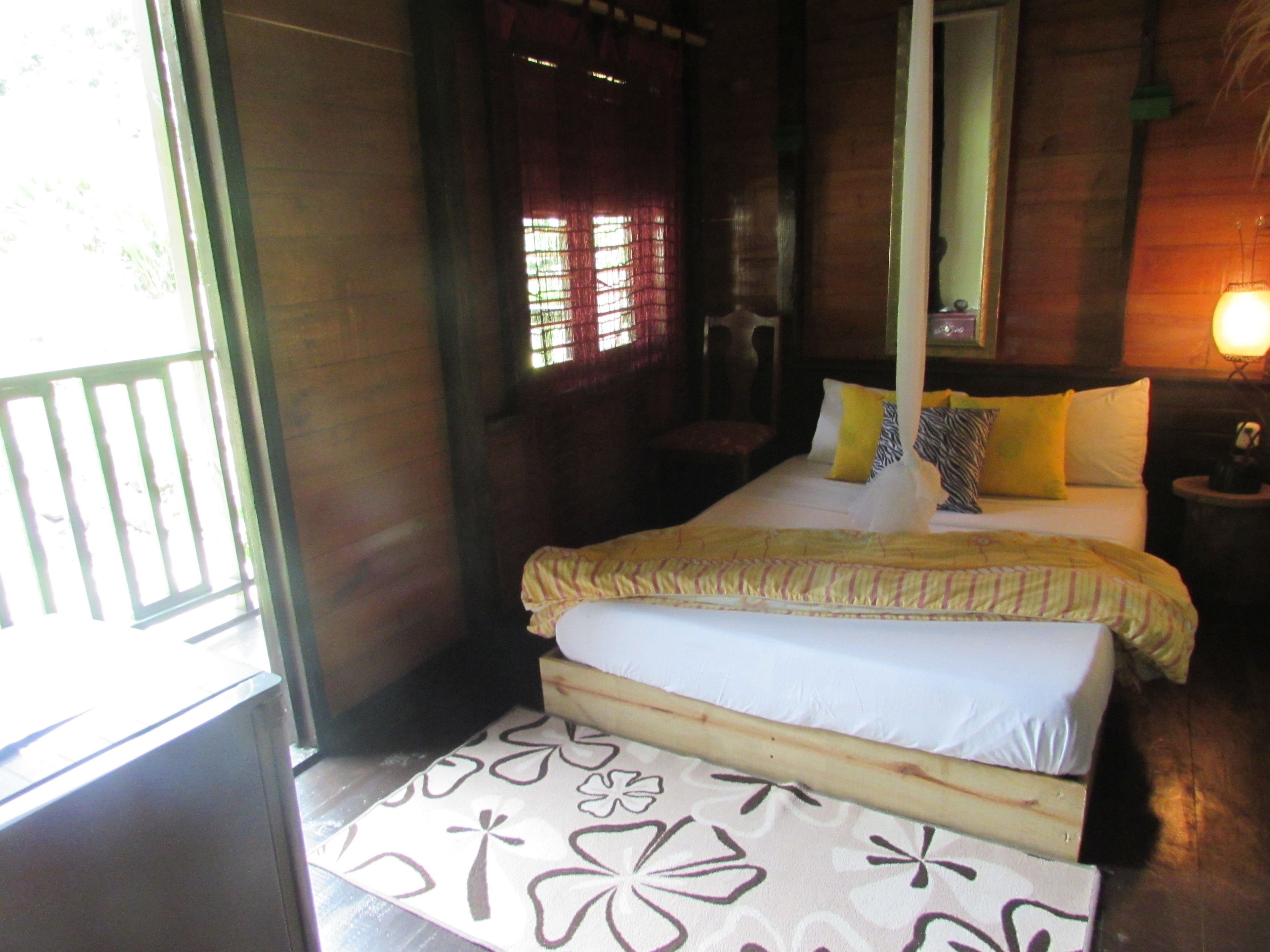 A bed with a canopy, a bedside table with a lamp, and a window with curtains.