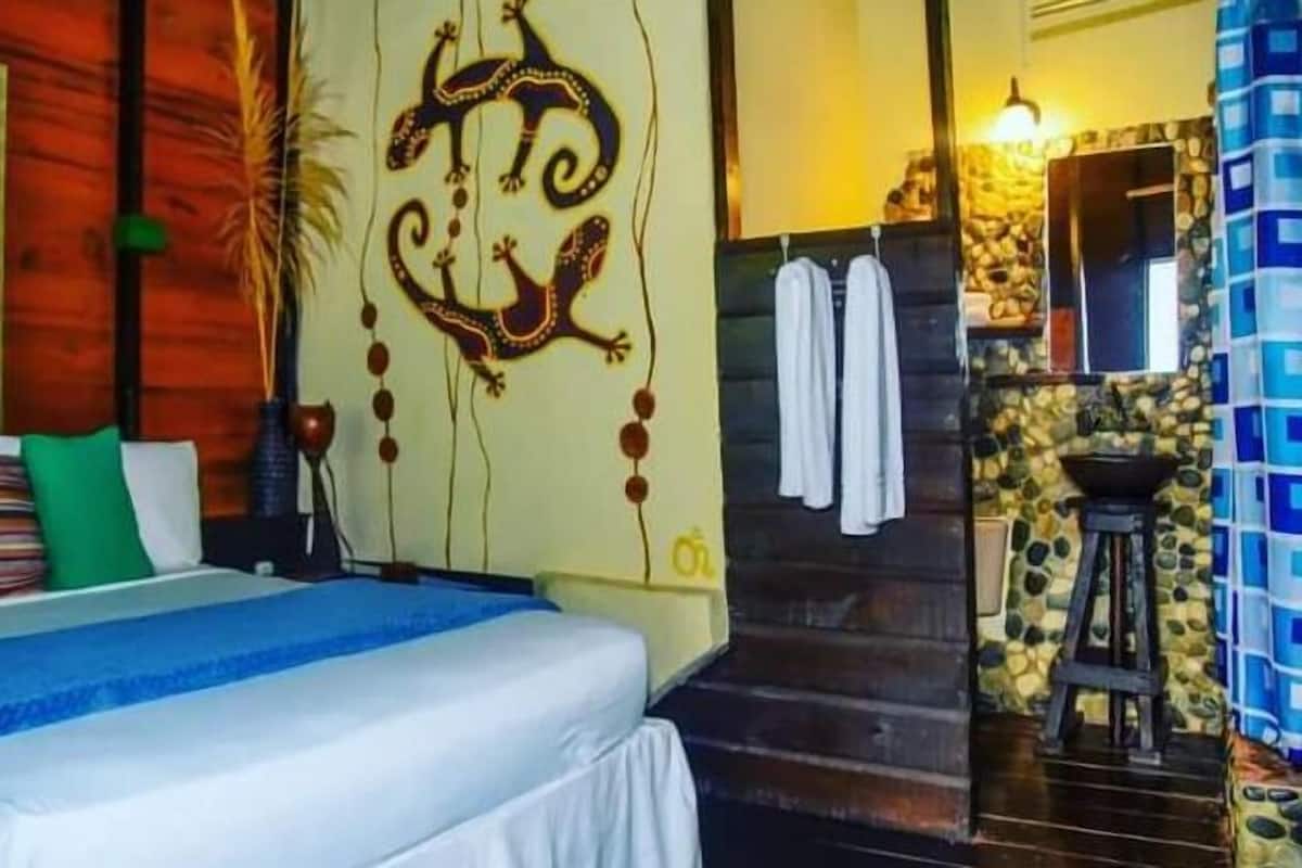 A bedroom with a bed, a wall with a decorative design, a bathroom with a sink and towels, and a staircase.