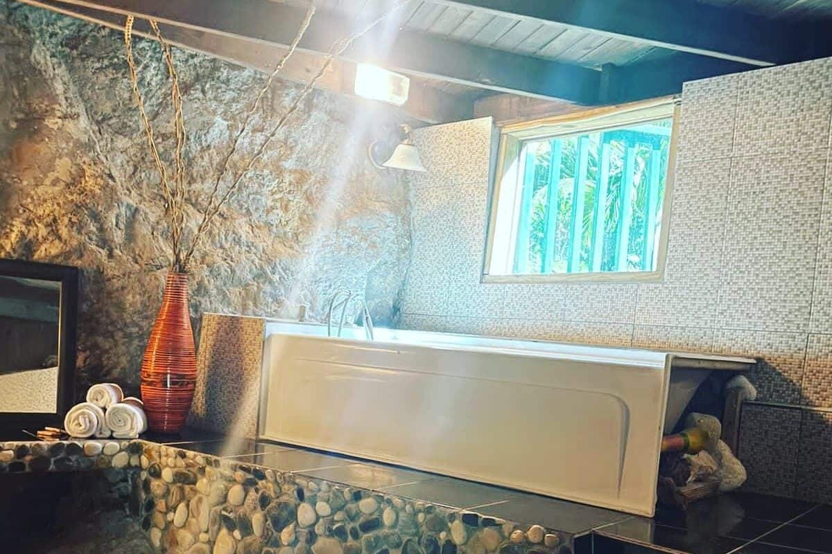 A bathroom with a stone wall, a window with a view, a sink, and a mirror.