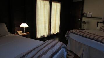 Una camera d'albergo con due letti, un comodino con una lampada e una finestra con tende.