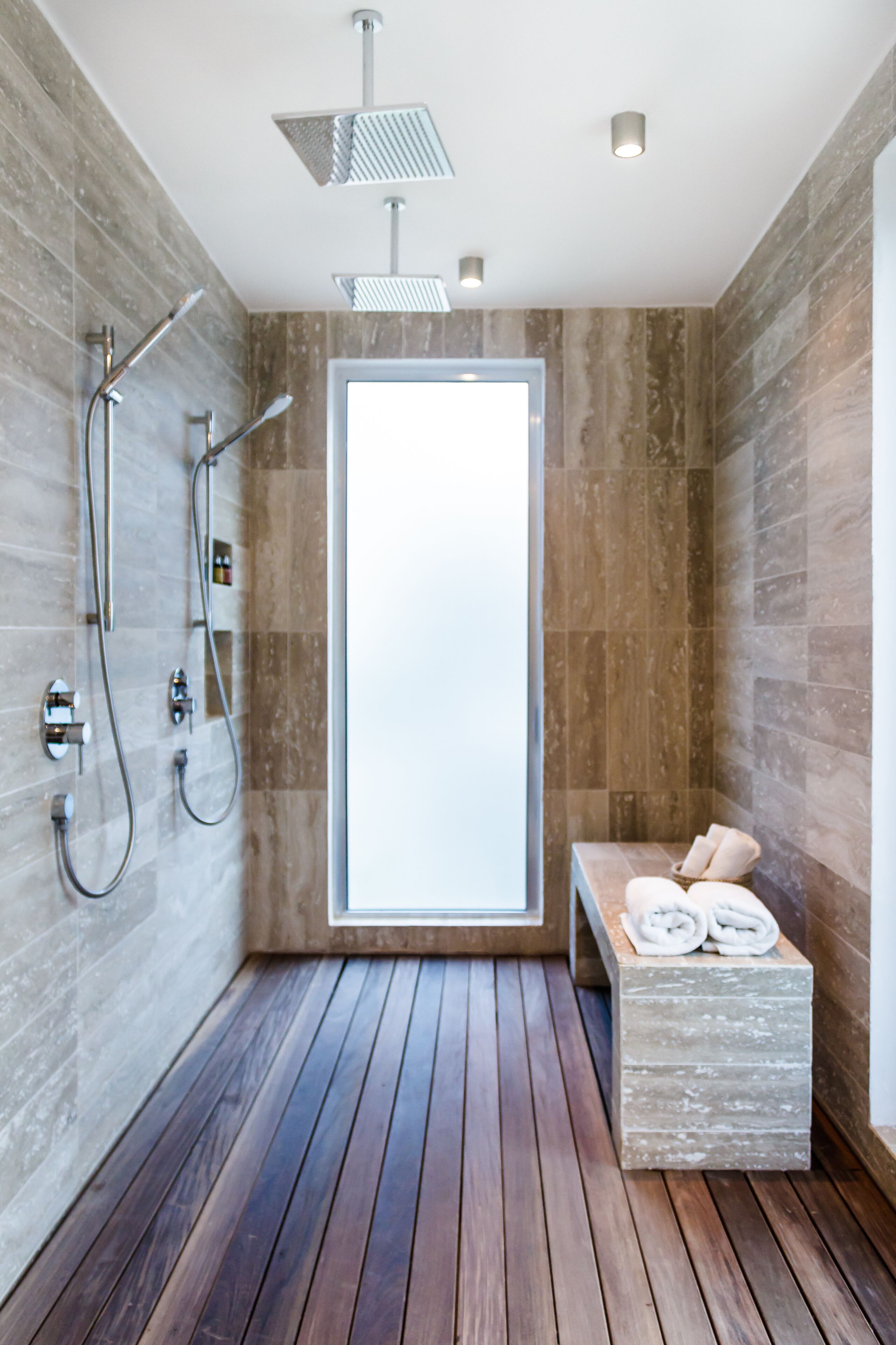 A modern bathroom with a wooden floor, a built-in bench with towels, and a large window.