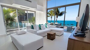A modern living room with a large window overlooking the ocean, white furniture, and a wooden coffee table.