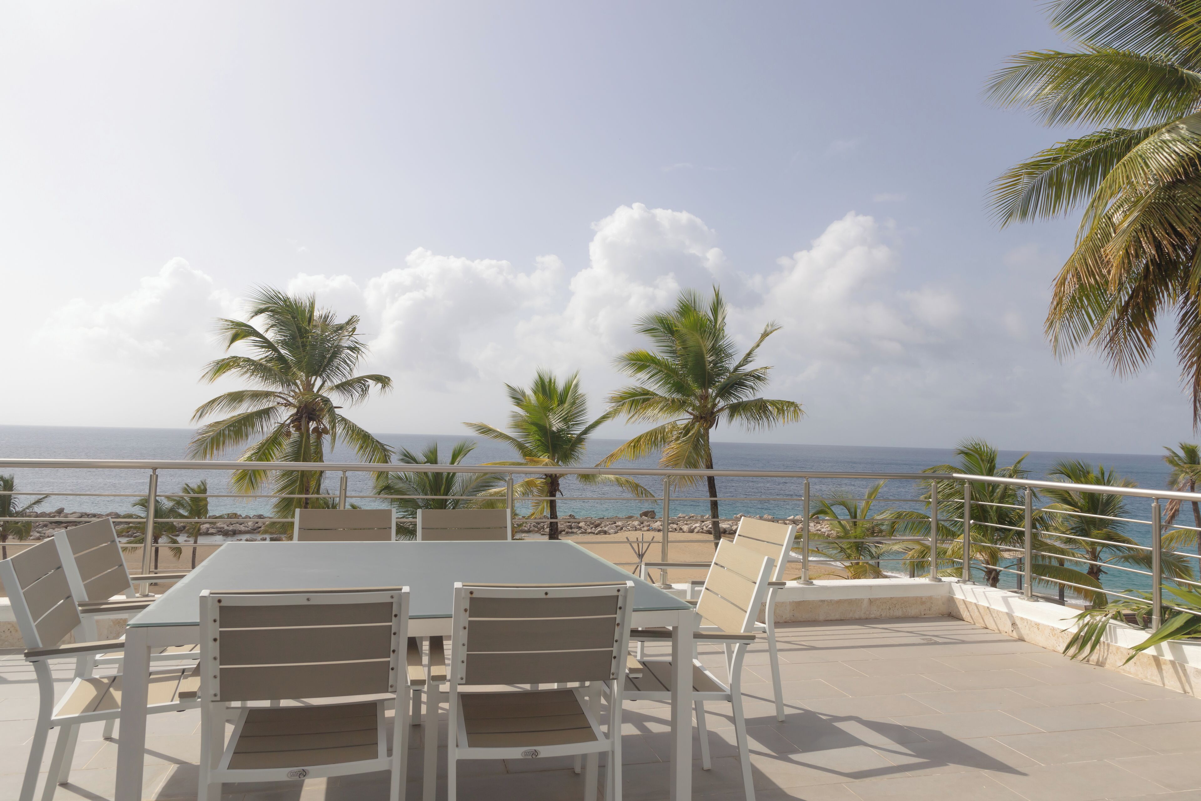 Une terrasse avec une table et des chaises, donnant sur une plage et l’océan.