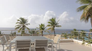 Une terrasse avec une table et des chaises, donnant sur une plage et l’océan.