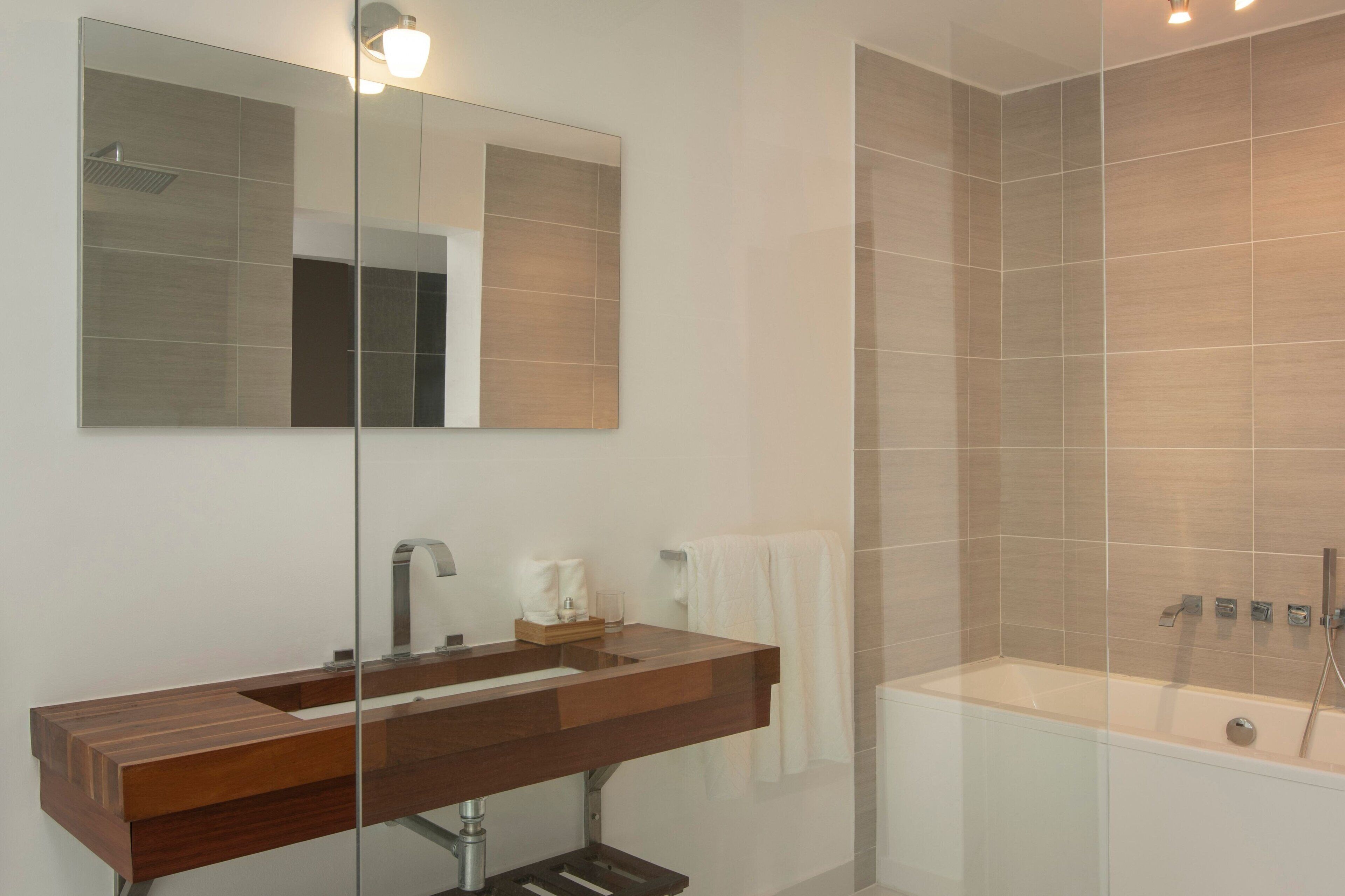 A modern bathroom with a wooden vanity, a large mirror, and a glass-enclosed bathtub.