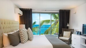 A hotel room with a large bed, a television, a white dresser, and a view of the ocean.