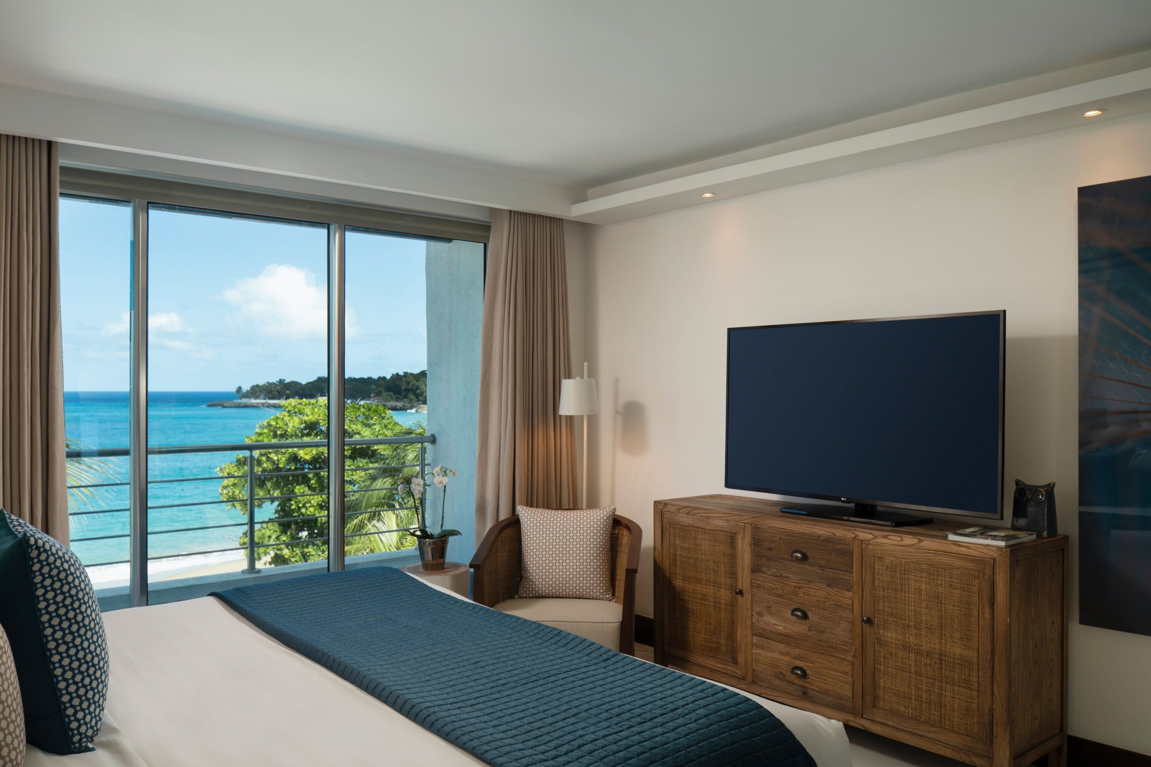Une chambre d’hôtel avec un grand lit, un téléviseur posé sur une commode en bois et une vue sur l’océan.