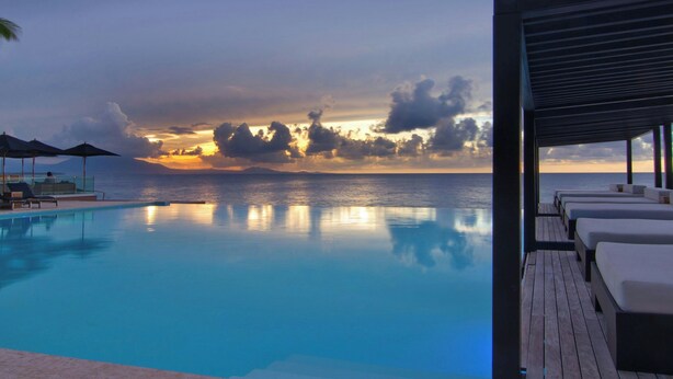 A poolside area with lounge chairs and a view of the ocean at sunset.