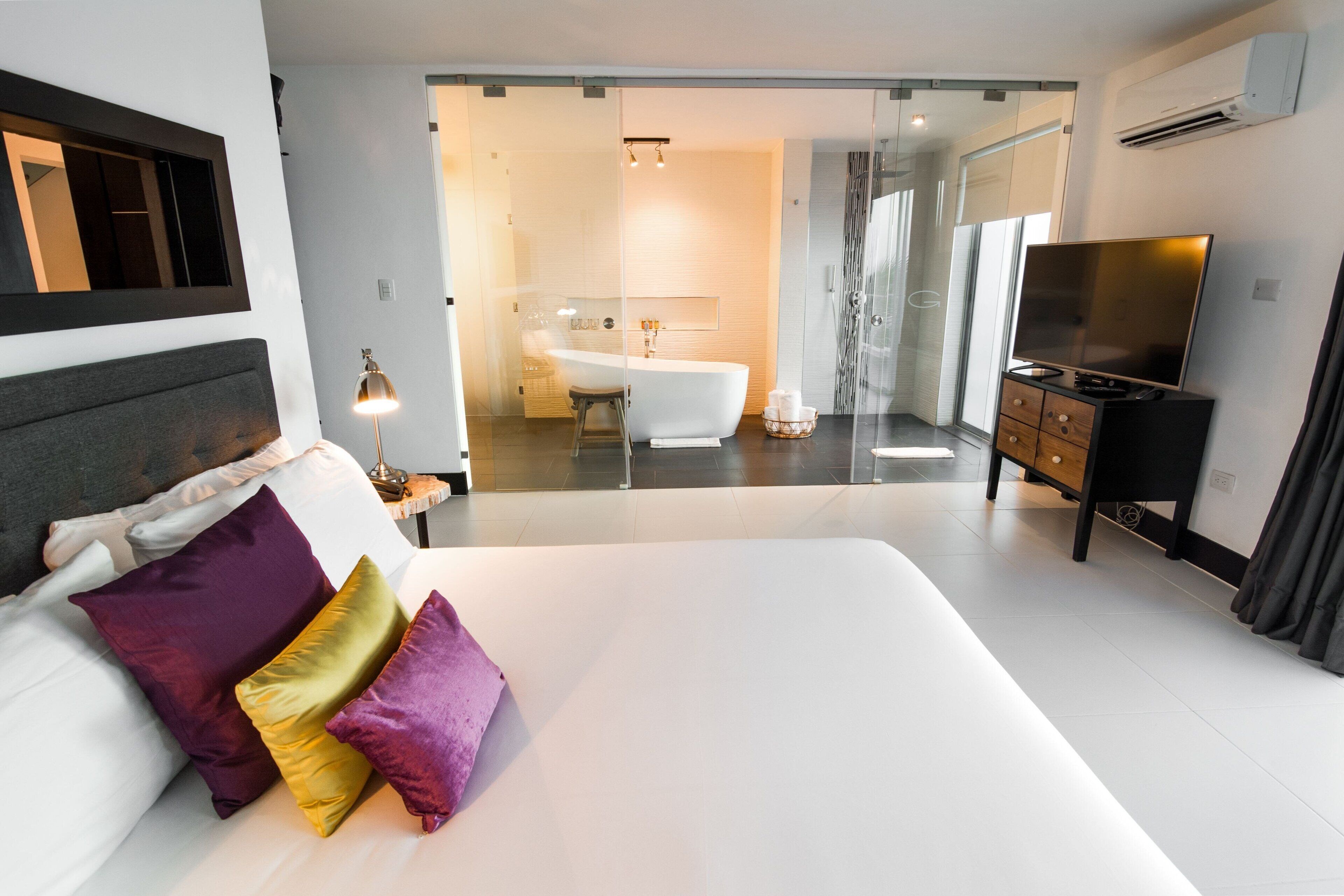 Ein modernes Hotelzimmer mit einem großen Bett, einem Fernseher, einem Badezimmer mit einer Badewanne und einer Glasabtrennung.