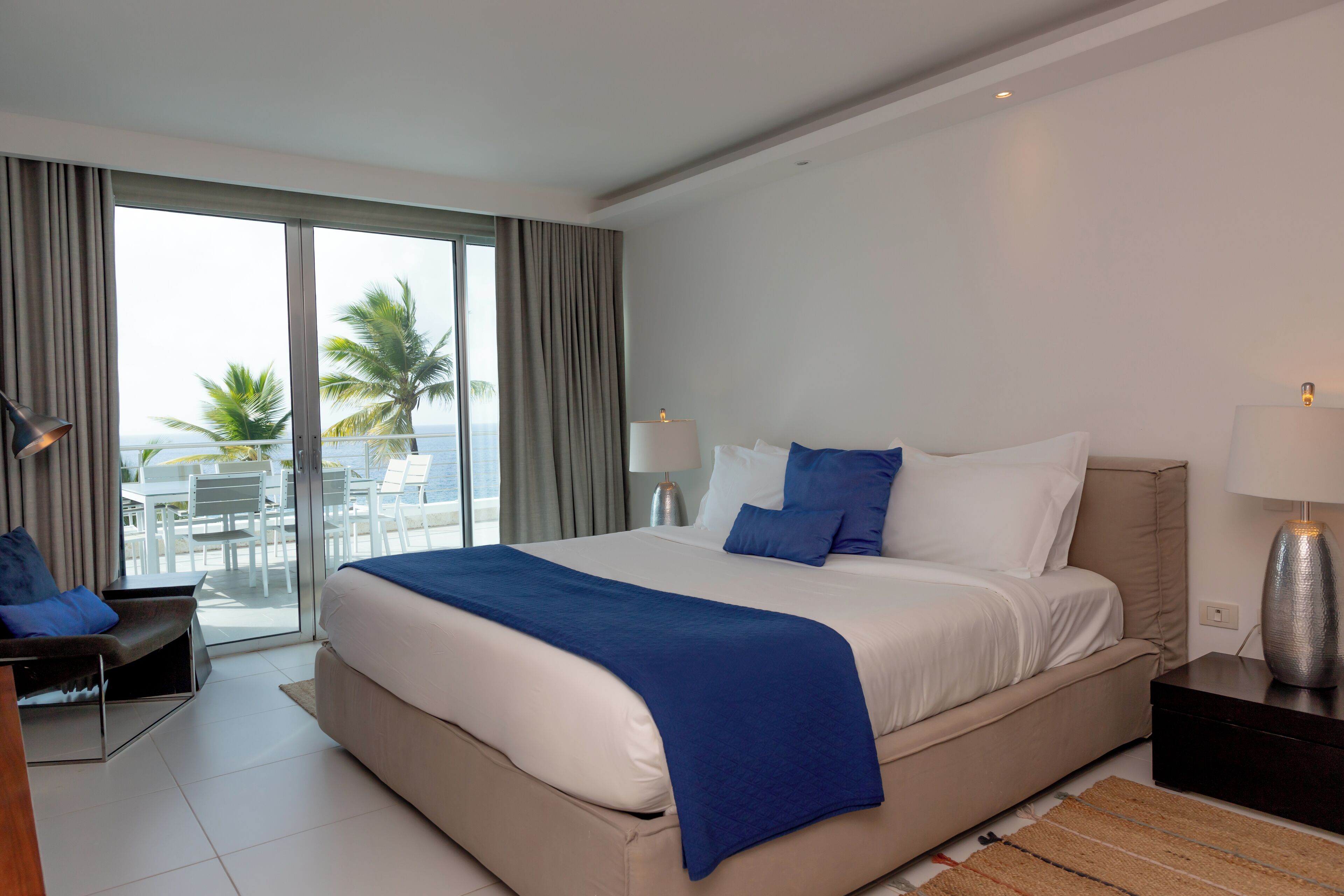 A modern hotel room with a large bed, a desk, and a view of the ocean.