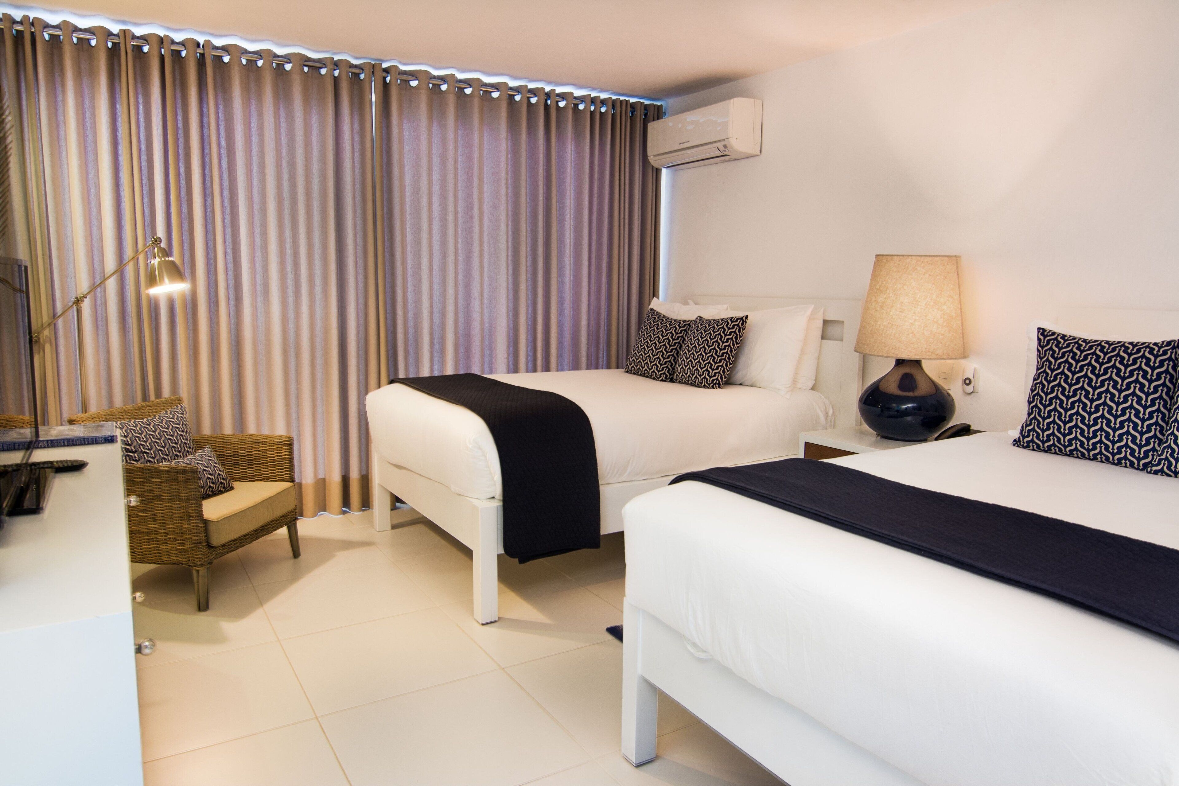 Una habitación de hotel con dos camas, una silla, una lámpara y aire acondicionado.