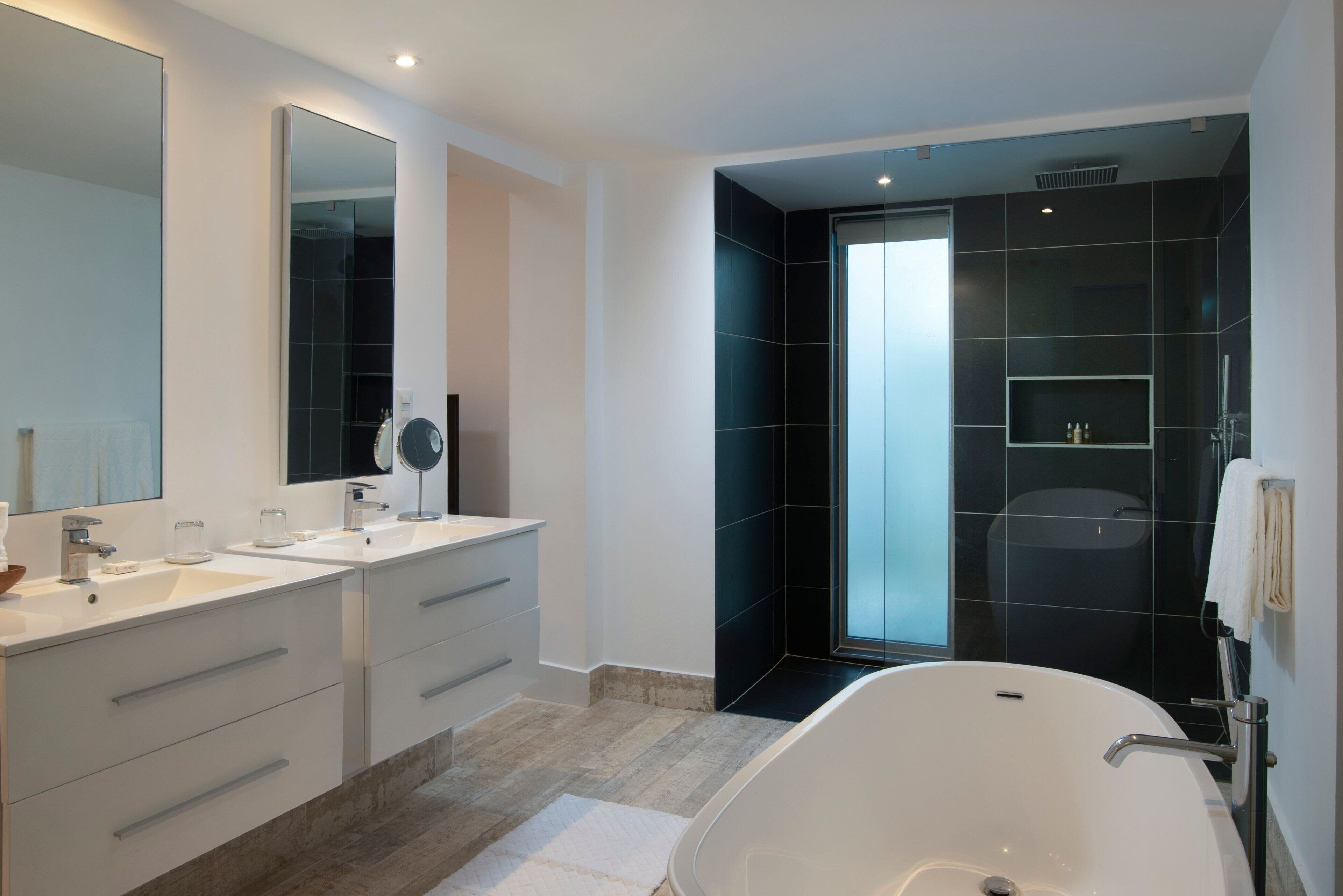 A modern bathroom with two sinks, a large mirror, a bathtub, and a glass-enclosed shower.