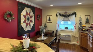A dining area with a red wall, a large quilt, and Christmas decorations. There is a window with a view of the outside. - Arthur's Country Inn (Arthur)