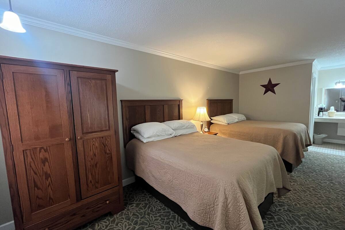 A hotel room with two beds, a wooden wardrobe, a star decoration on the wall, and a bathroom with a mirror and sink.