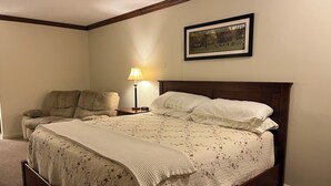 A bedroom with a large bed, a nightstand with a lamp, a chair, and a framed picture on the wall. - Arthur's Country Inn (Arthur)