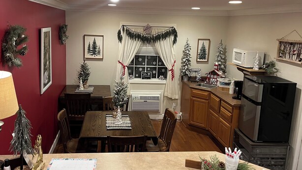 A dining area with a wooden table and chairs, a small Christmas tree, and a window with curtains. - Arthur's Country Inn (Arthur)