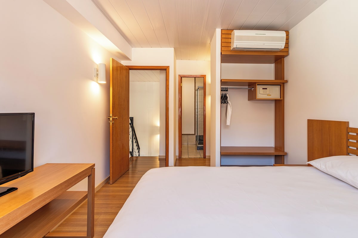 Une chambre d’hôtel avec un lit, une télévision, un bureau en bois, une armoire et une salle de bain visible à travers une porte ouverte.