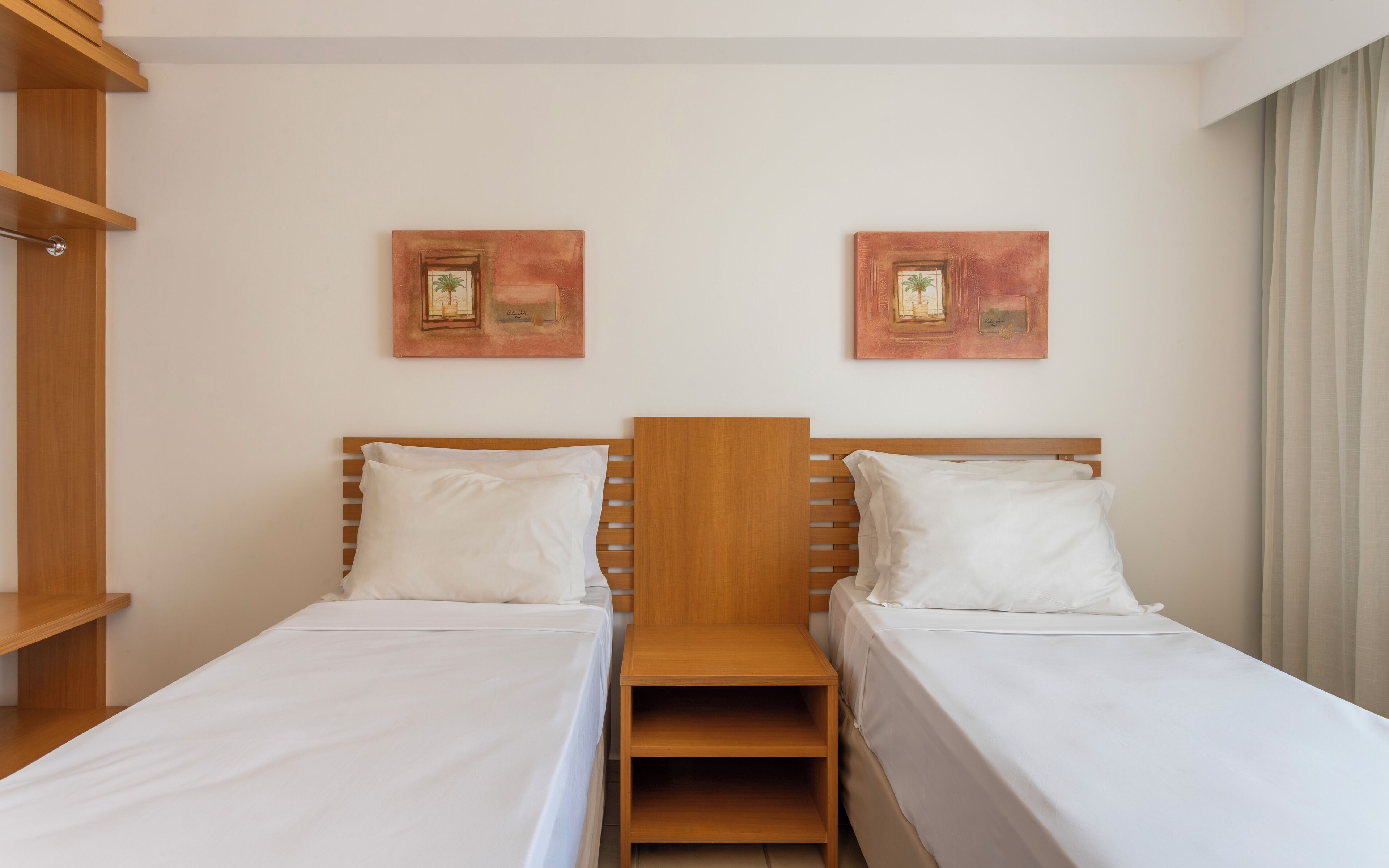 A hotel room with two single beds, wooden headboards, white bedding, and two framed artworks on the wall.