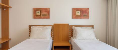 A hotel room with two single beds, wooden headboards, white bedding, and two framed artworks on the wall.