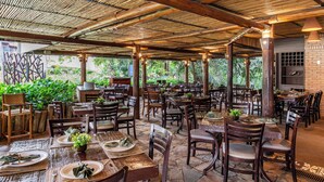 An outdoor restaurant with bamboo ceiling, wooden tables, and chairs, surrounded by greenery. - Rio Quente Resorts - Hotel Giardino (Rio Quente)